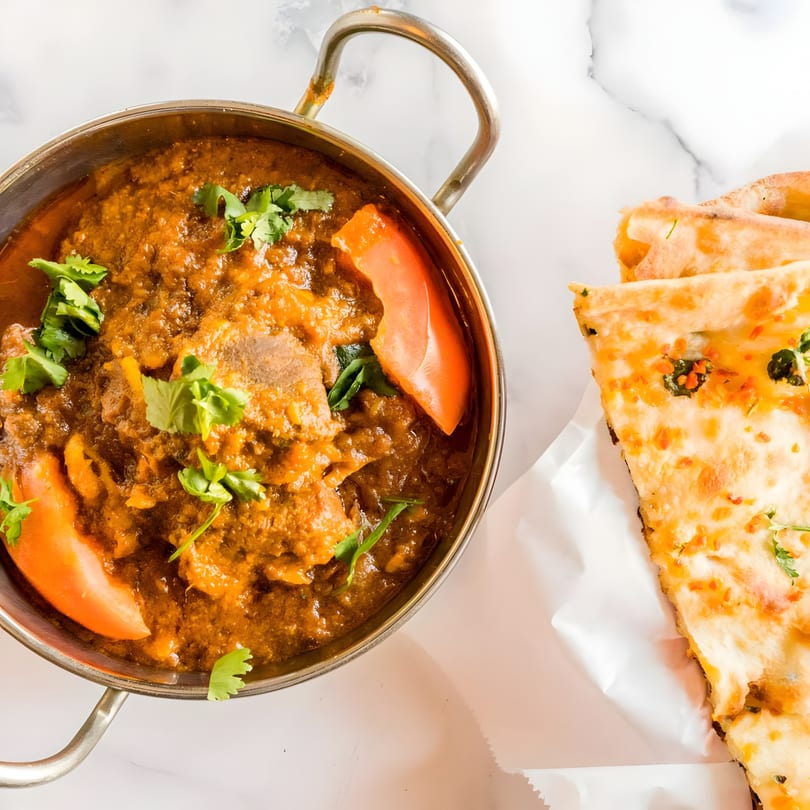 A kadai of Punjabi Dhaba Dixon's chicken curry with tomatoes and cilantro, served with naan.