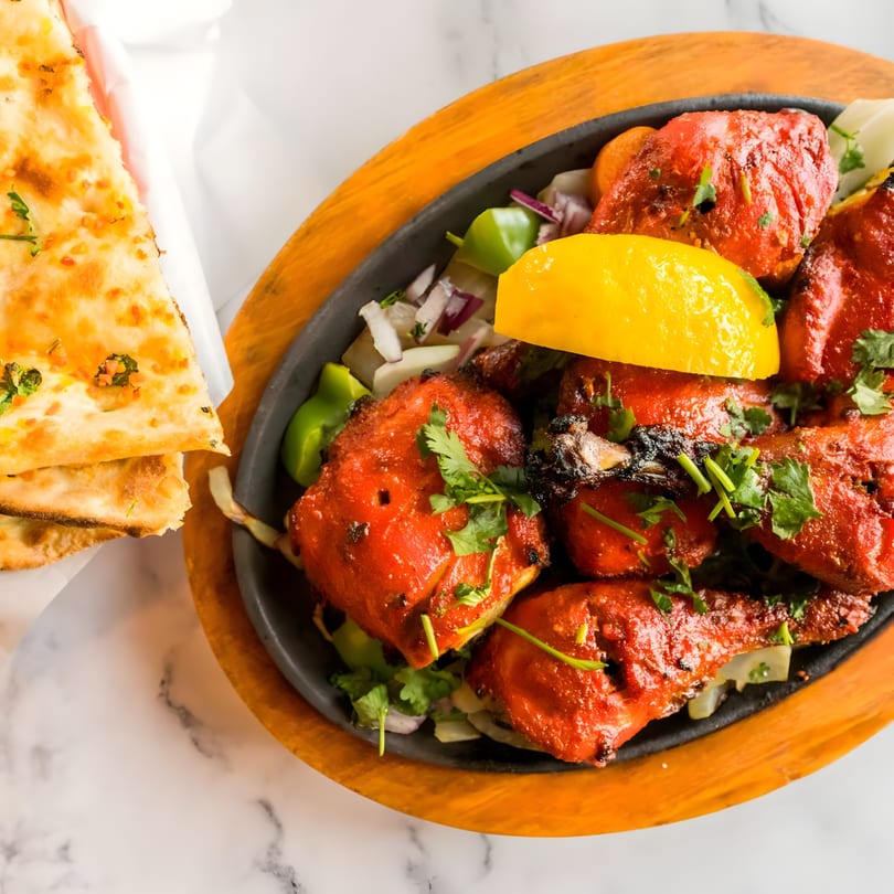 Tandoori chicken with lemon, cilantro, and onions in a cast iron skillet, with naan bread.