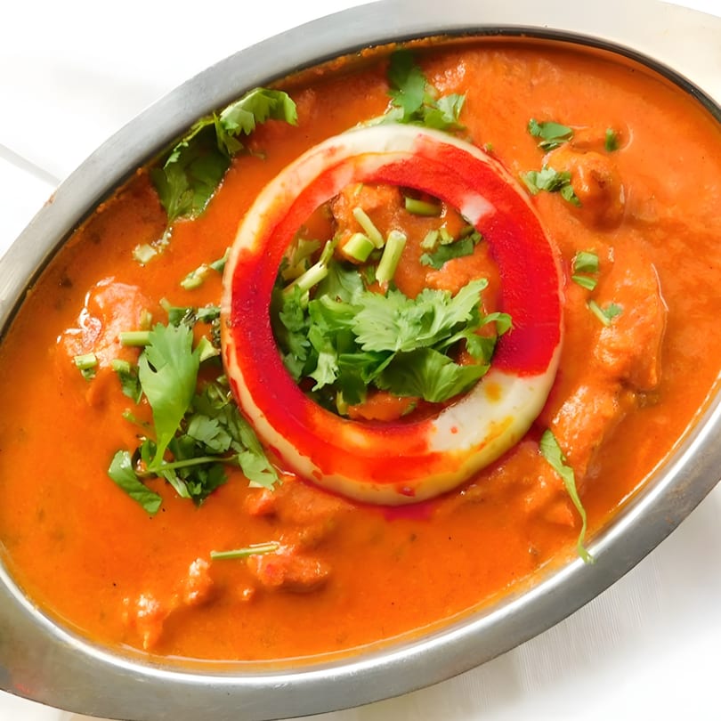Indian butter chicken in a silver serving dish, garnished with cilantro and a red-stained onion ring.